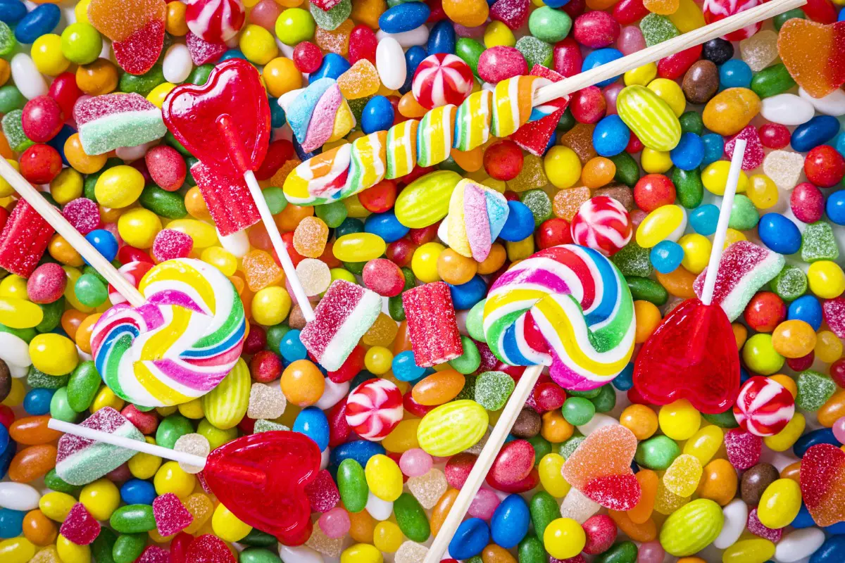 An assortment of colorful candies, including lollipops, gummy hearts, and various chewy sweets, scattered across the image.