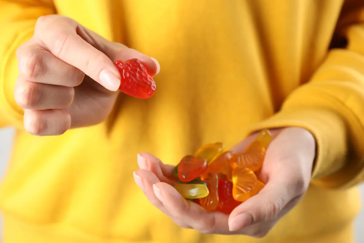 A person in a yellow sweater holds gummy bears, picking up a red one with their right hand.
