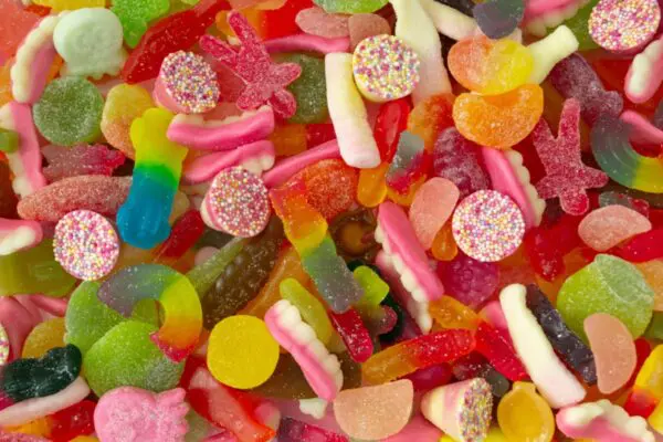 A colorful assortment of various gummy candies, including gummy worms, jelly beans, and round candies with sprinkles, scattered randomly.